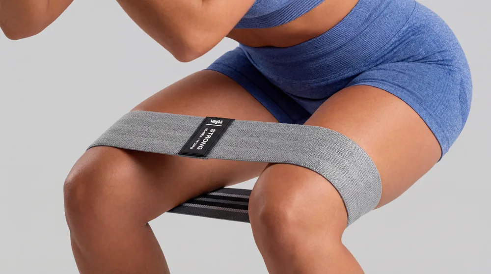 A fabric band worn flat just above both knees during a squat, with the knees pushed out against it